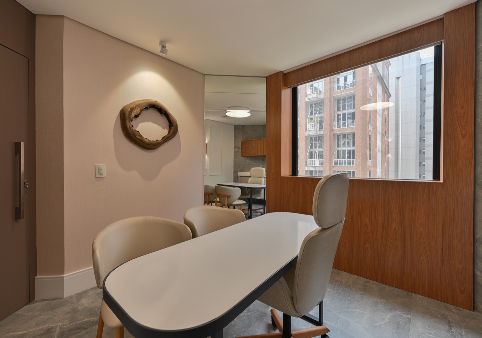 Sala de consulta do consultório, com mesa oval clara, cadeiras estofadas e janela para os prédios da Vila Olímpia