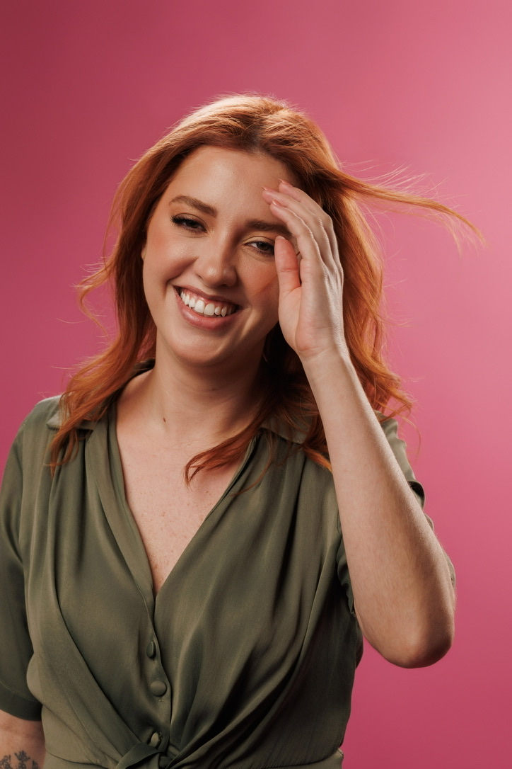 Dra. Eduarda Coelho rindo, com a mão no cabelo ruivo
